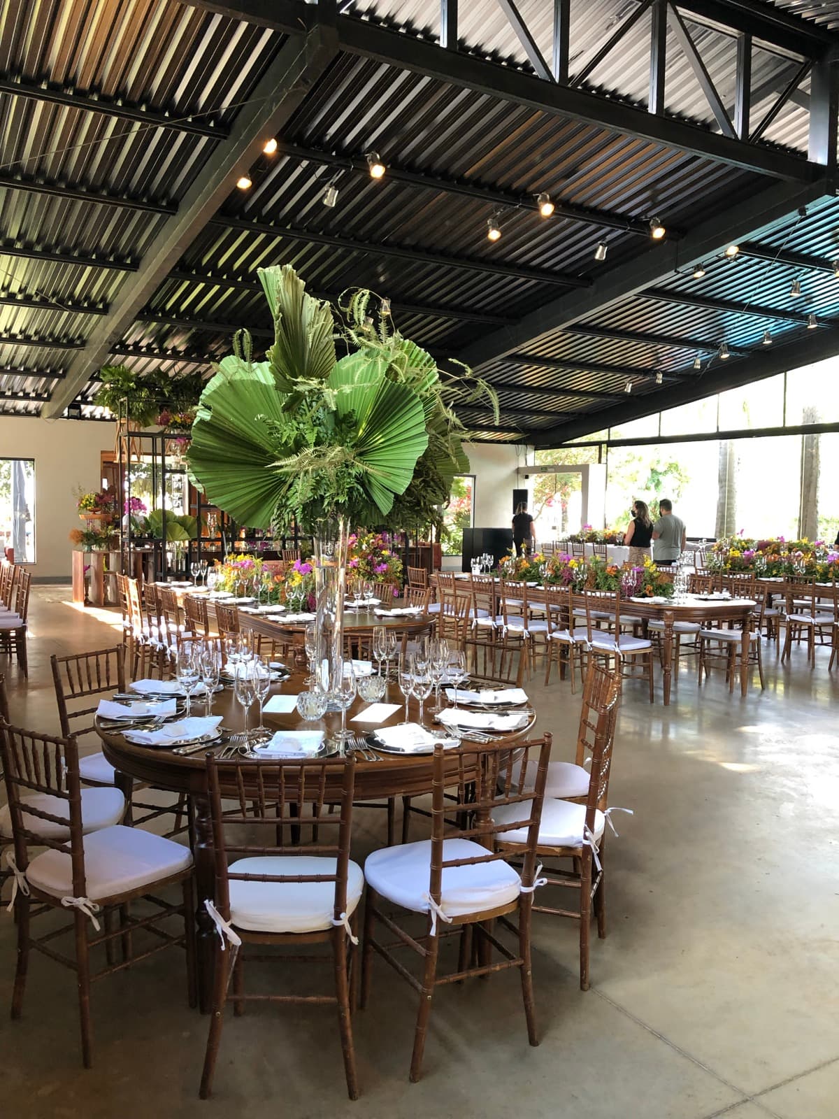 Salão novo montado para casamento com mesas redondas e flores